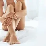 Photo of a woman sitting on a bed with her legs crossed