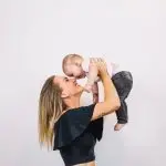 Photo of a mother wearing a black top holding her child up, wondering "What is a Mommy Makeover?"