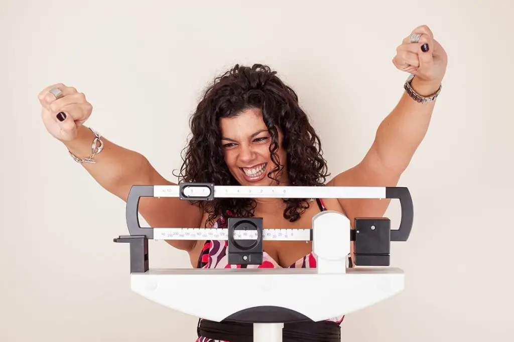 Women on Scale with arms raised in happiness for meeting her 2020 weight loss goal.