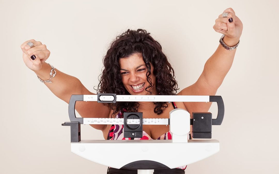 Women on Scale with arms raised in happiness for meeting her 2020 weight loss goal.