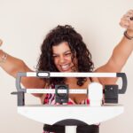 Women on Scale with arms raised in happiness for meeting her 2020 weight loss goal.