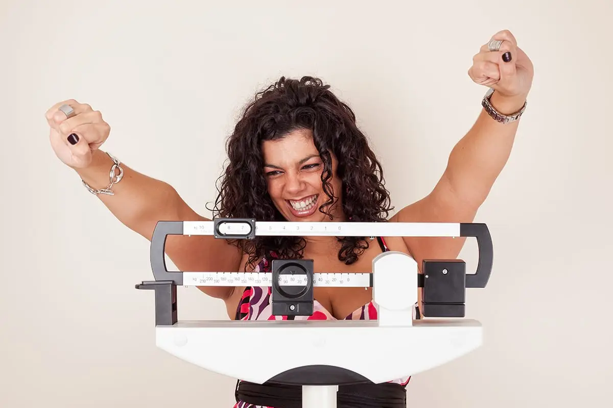 Women on Scale with arms raised in happiness for meeting her 2020 weight loss goal.