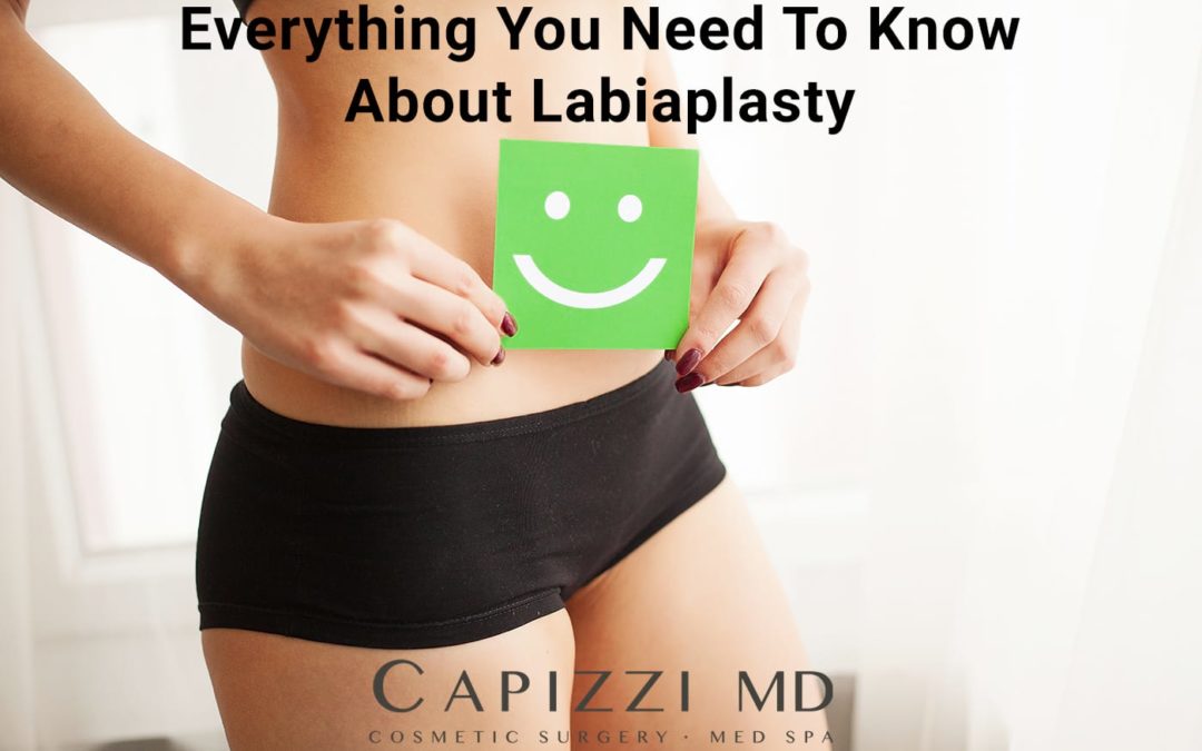 Women in black shorts holding green smiley face with text "Everything You Need To Know About Labiaplasty" and Capizzi MD logo