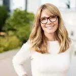 Woman in front of house is white sweater enjoying her breast augmentation without an implant.