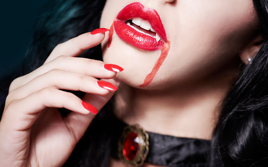 Cose-up of young beautiful woman's face dressed for Halloween and wearing vampire fangs.