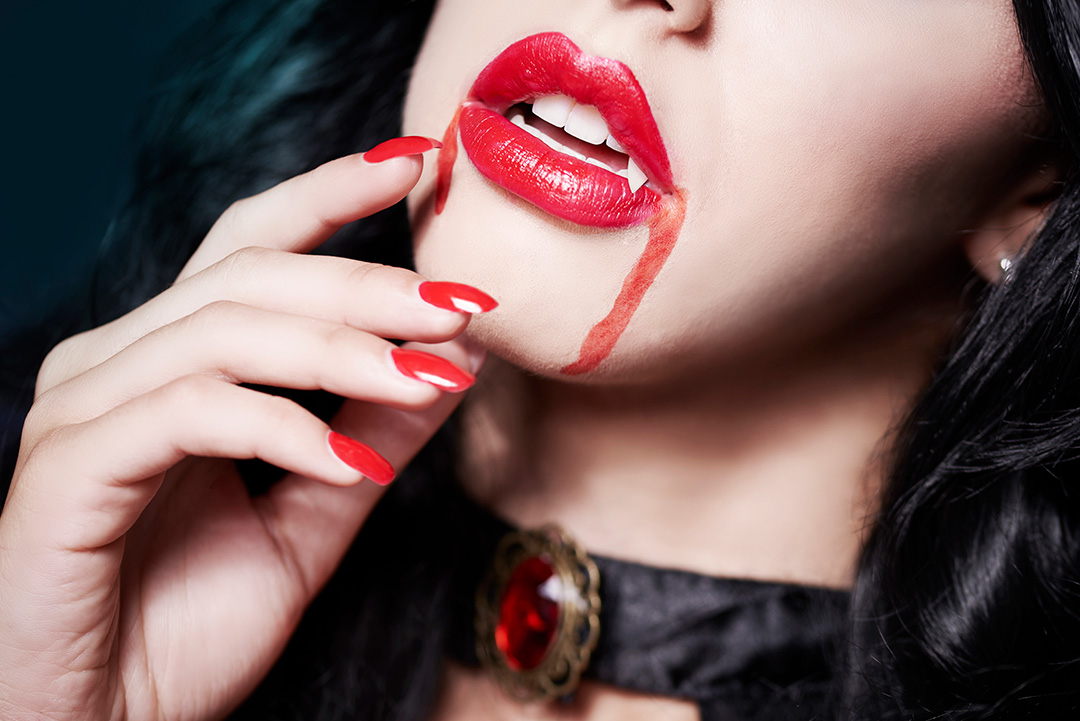 Cose-up of young beautiful woman's face dressed for Halloween and wearing vampire fangs.