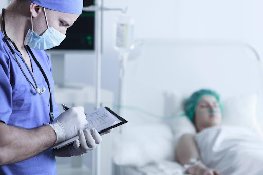 A doctor charting notes next to a woman recovering after breast augmentation surgery.