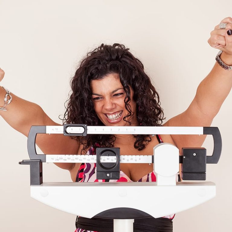 Women on Scale with arms raised in happiness for meeting her 2020 weight loss goal.